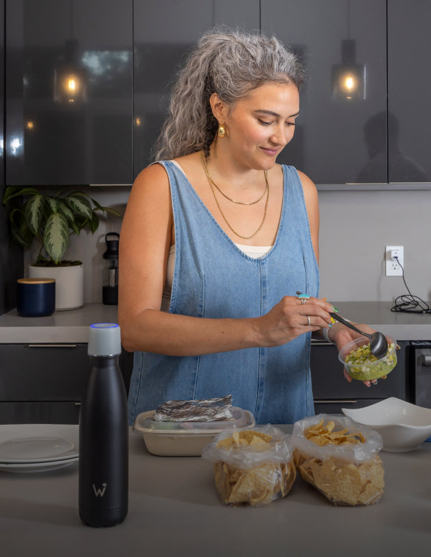 Woman preparing food in kitchen and Water.io bottle sitting on counter